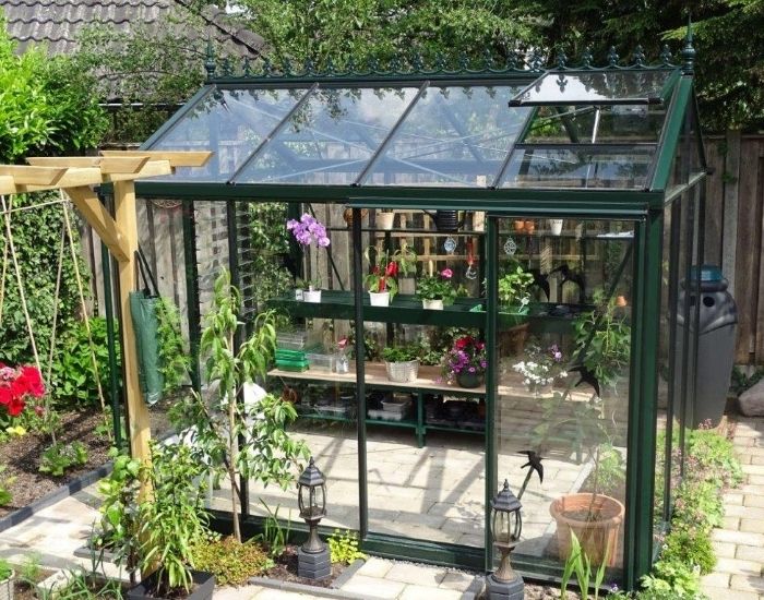 Impressie van een groene tuin met een kleine tuinkas, voorzien van Victoriaanse nok.